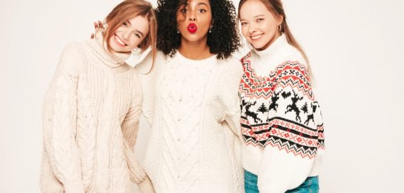 Three young beautiful smiling hipster girls in trendy winter sweaters. Sexy carefree women in studio. Positive models having fun and hugging